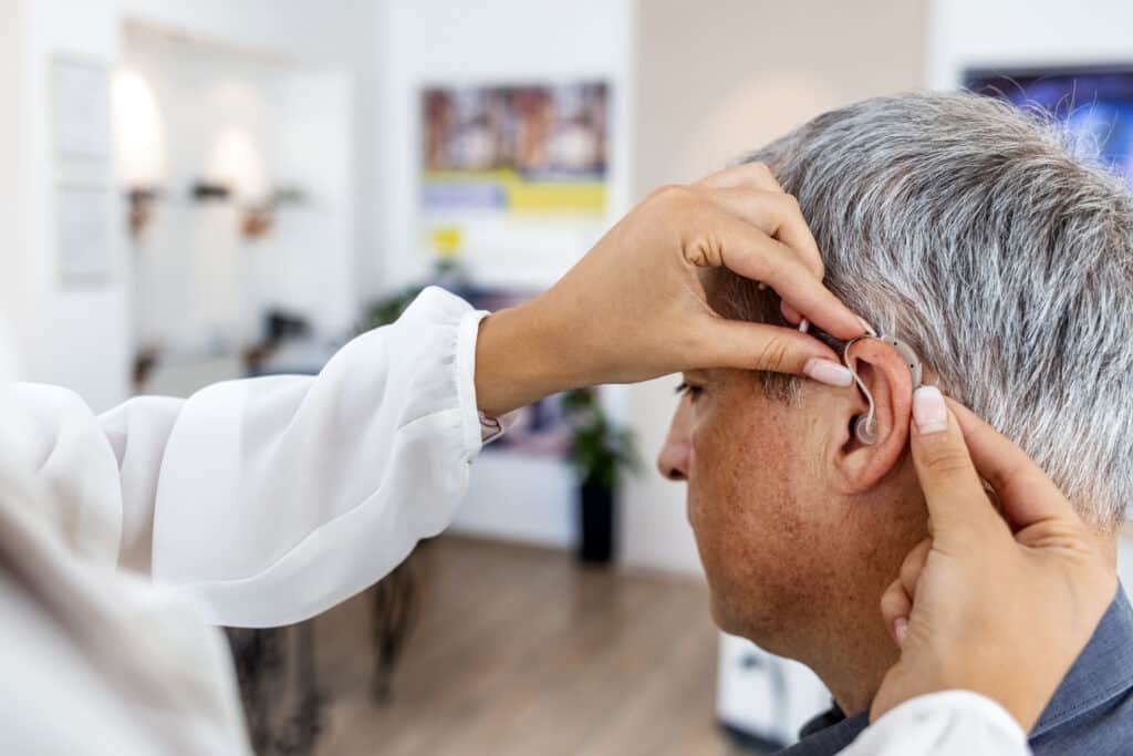 A doctor fits a hearing aid inside a man's ear.