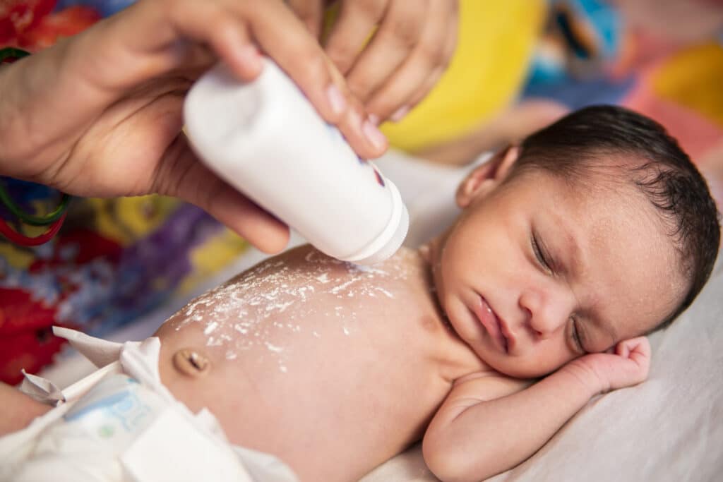 A mother applying talcum powder on her baby's chest.